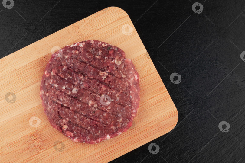 Скачать Сырые котлеты для гамбургеров на деревянной разделочной доске на черном фоне фотосток Ozero