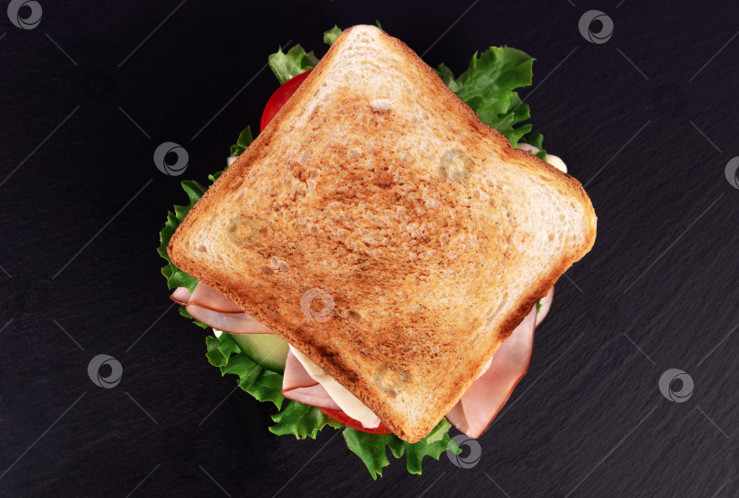 Скачать Вкусный сэндвич с ветчиной, свежим салатом и маринованным огурцом подается на каменной доске. Вид сверху. фотосток Ozero