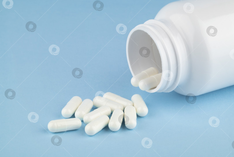 Скачать Различные лекарства и таблетки с добавками для здоровья, высыпанные из белого флакона с лекарством, вид сверху на цветном синем фоне. фотосток Ozero
