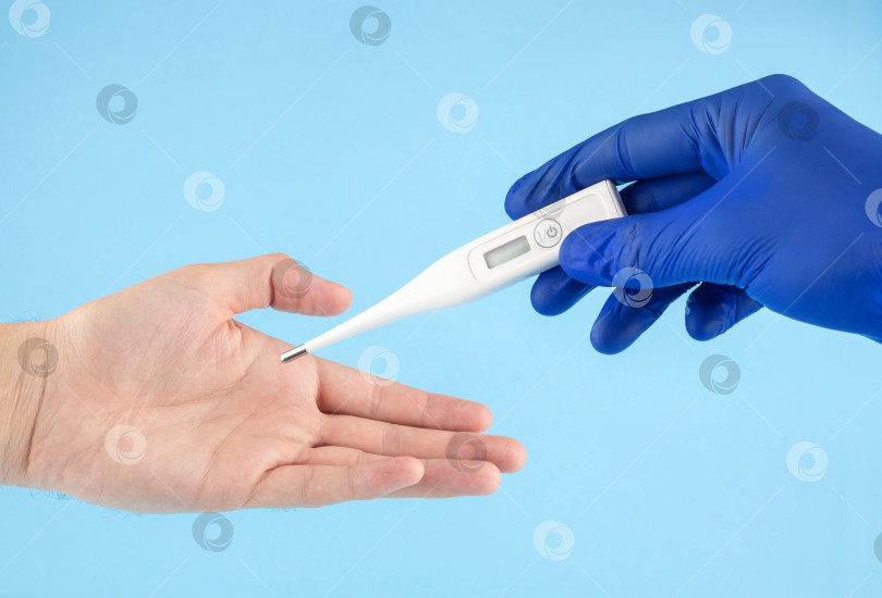 Скачать Врач в синих латексных перчатках передает цифровой термометр в руки пациента. Измерение температуры тела. фотосток Ozero
