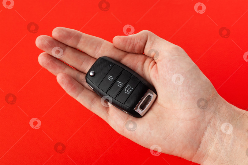 Скачать Мужская рука держит ключи от машины, выделенные крупным планом на красном фоне. фотосток Ozero