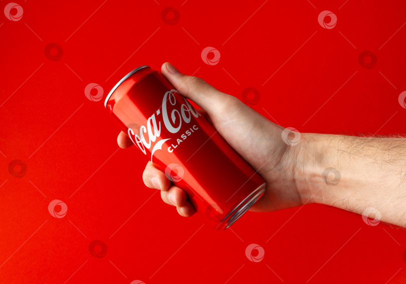 Скачать БАТУМИ, ГРУЗИЯ, 15.03.2023: Холодная банка coca-cola в руке на красном фоне. фотосток Ozero