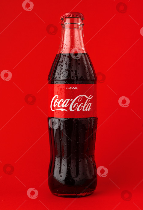 Скачать БАТУМИ, ГРУЗИЯ, 15 03 2023: Холодная стеклянная бутылка coca-cola с капельками воды на красном фоне. фотосток Ozero