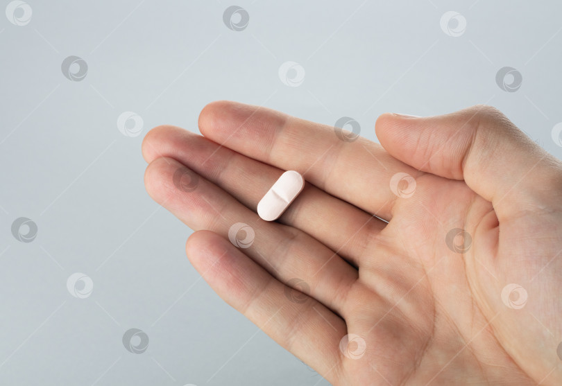 Скачать Мужская рука, держащая в руке одну таблетку на сером фоне, принимает ваше лекарство. Закрыть фотосток Ozero