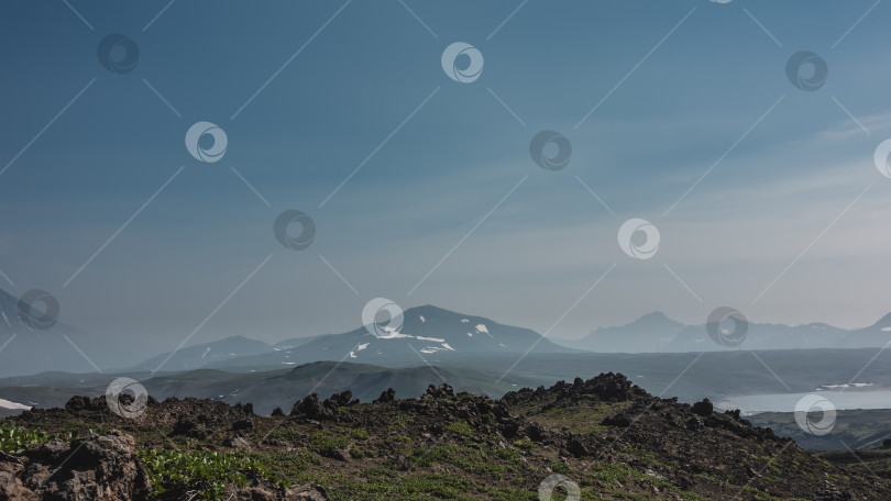 Скачать Вулканические породы разбросаны по склону горы. Редкая растительность на земле. фотосток Ozero