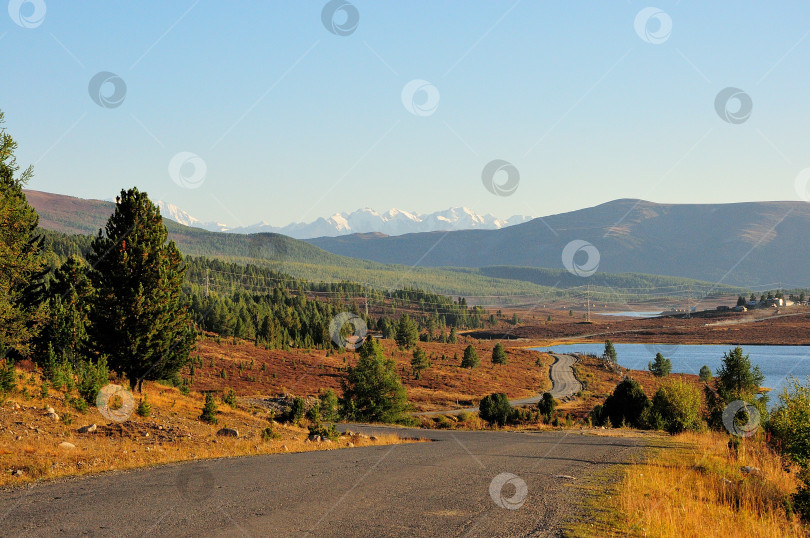 Скачать Красивая лесная дорога, идущая через осеннюю горную тундру вдоль берега озера на фоне заснеженных вершин. фотосток Ozero