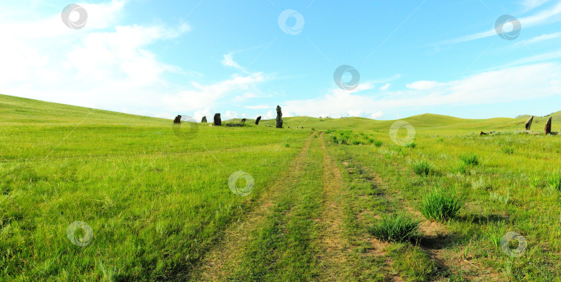 Скачать Полевая дорога, ведущая через большое поле в степи у холмов к древним каменным менгирам. фотосток Ozero