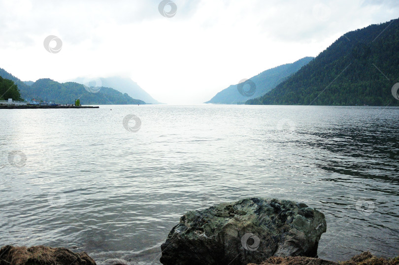 Скачать Вид со скалистого берега большого озера, лежащего в горах, в пасмурную погоду. фотосток Ozero