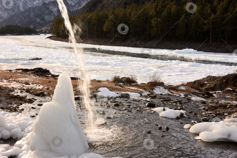 Скачать Поток воды стекает к ледяной глыбе на берегу красивой горной реки в заснеженной долине. фотосток Ozero