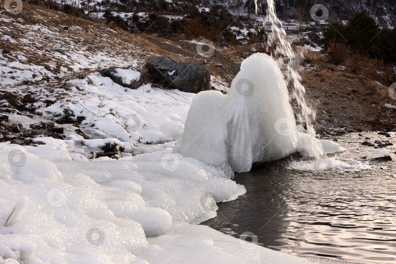 Скачать Ледяная глыба и струящийся по ней поток воды на фоне красивой реки, окруженной заснеженными зимними горами. фотосток Ozero