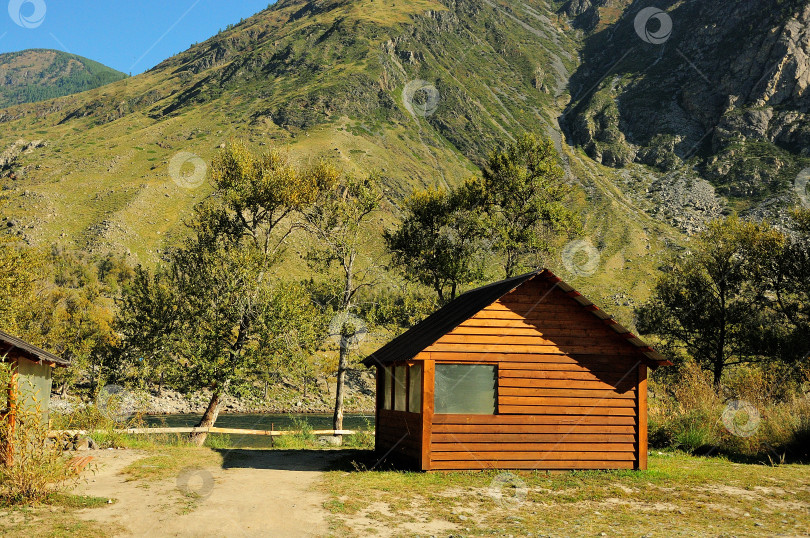 Скачать Небольшой деревянный домик с окнами спрятан вдоль тропинки, ведущей к берегу горной реки. фотосток Ozero