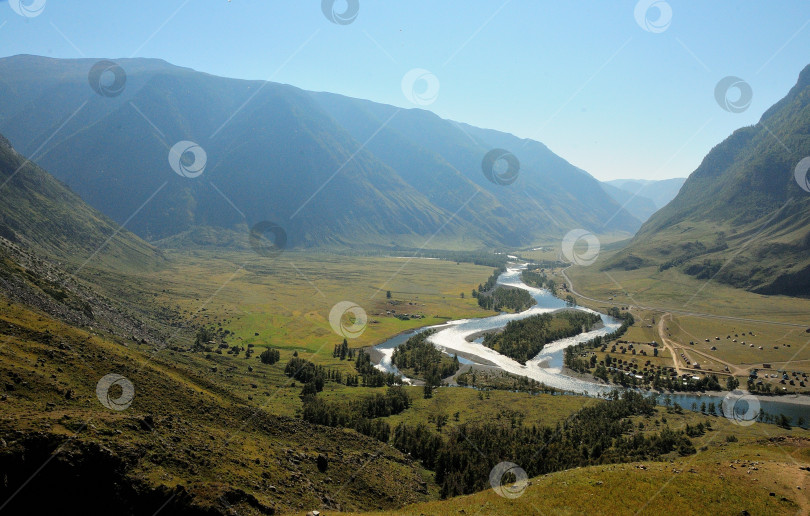 Скачать Живописная долина, залитая солнечным светом, окруженная горами и текущей извилистой рекой. фотосток Ozero