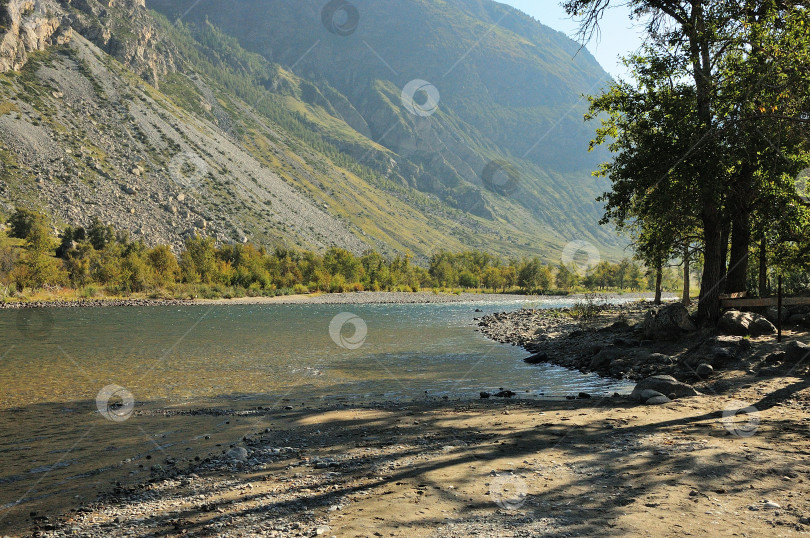 Скачать Скалистый берег красивой реки у подножия горы в лучах восходящего солнца. фотосток Ozero