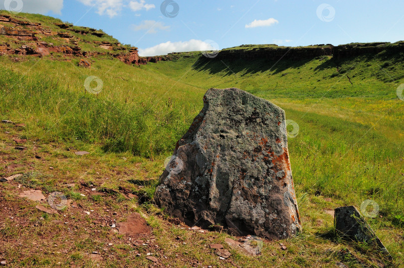 Скачать Менгир, надгробная плита древнего захоронения у склона высокой горы в летней степи. фотосток Ozero