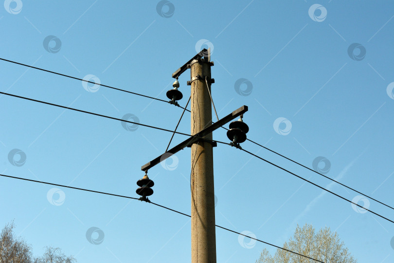 Скачать Верхушка железобетонного столба с проходящей линией электропередачи на фоне голубого ясного неба. фотосток Ozero