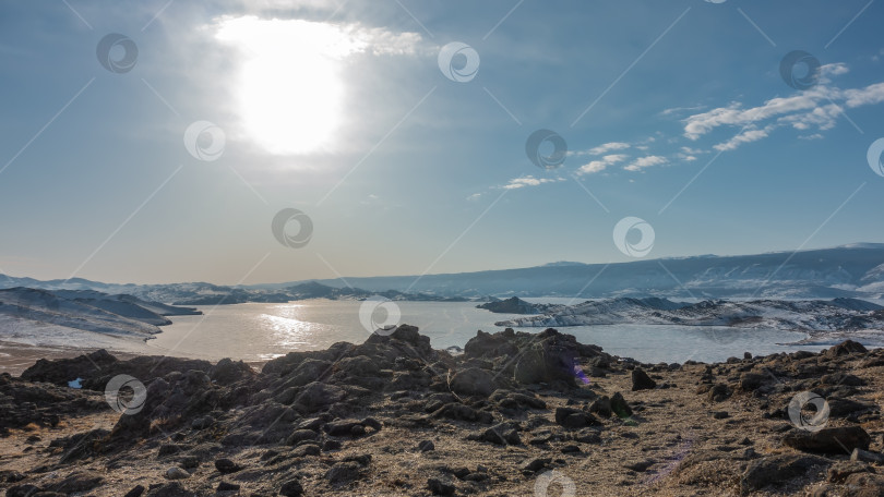 Скачать Замерзшее озеро окружено заснеженными холмами. Солнце сияет в голубом небе. фотосток Ozero