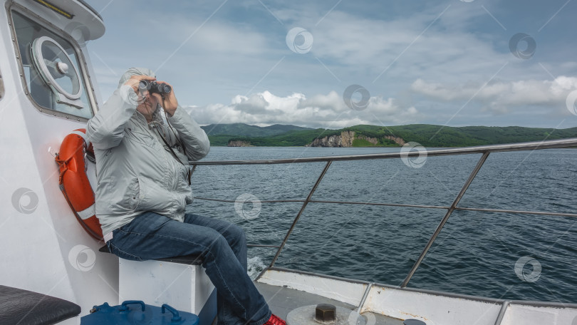 Скачать Яхта в Тихом океане. Мужчина сидит рядом с металлическими перилами и смотрит в бинокль. фотосток Ozero