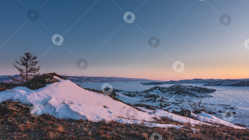 Скачать Рассвет в Сибири зимой. На земле лежит снег и сухая трава.  Солнечные блики на льду замерзшего озера Байкал. фотосток Ozero