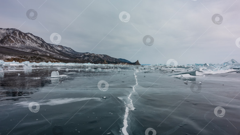 Скачать На гладкой поверхности замерзшего озера видна глубокая трещина, разбросаны осколки льда. фотосток Ozero