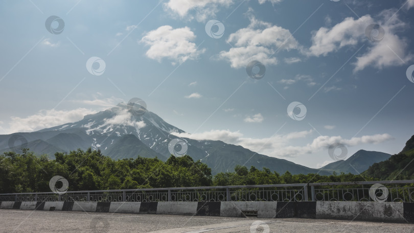 Скачать Красивый конусообразный вулкан на фоне голубого неба.  На переднем плане - зеленый лес, шоссе фотосток Ozero