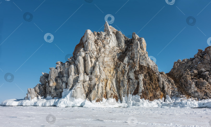 Скачать Живописная гранитная скала, лишенная растительности, возвышается над замерзшим озером. фотосток Ozero