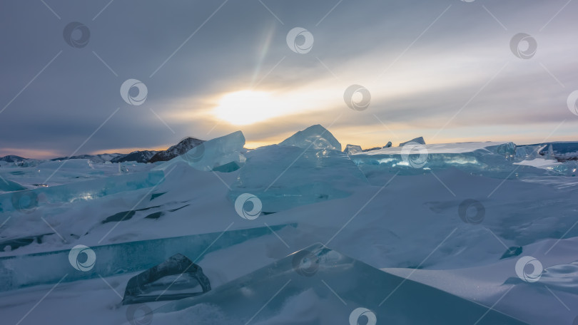Скачать Глыба бирюзового льда возвышается на замерзшем озере. Заходящее солнце на облачном небе. Блики по краям. Байкал. фотосток Ozero
