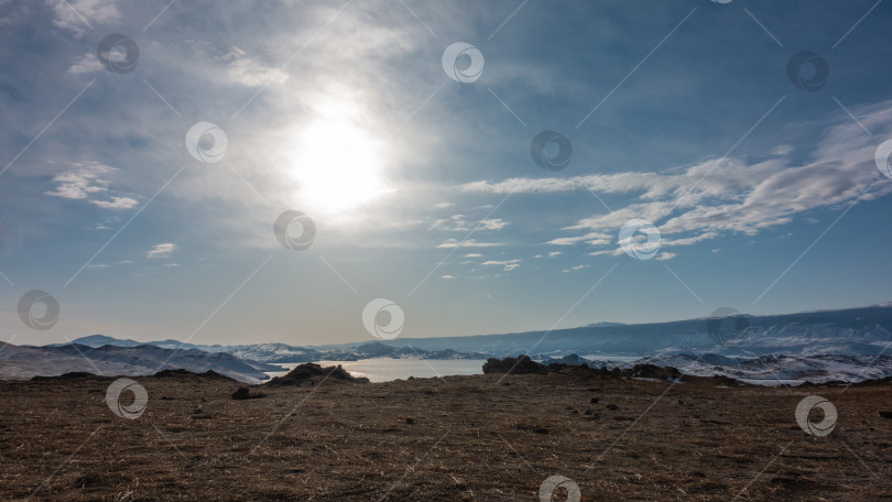 Скачать Замерзшее озеро окружено заснеженными горами. Солнце сияет в голубом небе. фотосток Ozero