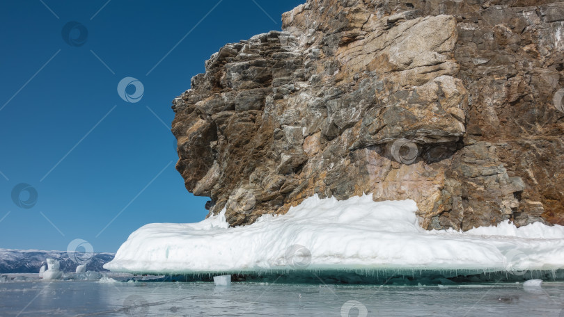 Скачать Причудливая гранитная скала, лишенная растительности, возвышается над замерзшим озером. фотосток Ozero