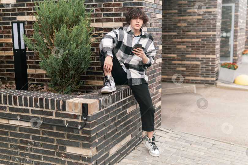 Скачать молодой человек в городском пейзаже сидит на бордюре фотосток Ozero
