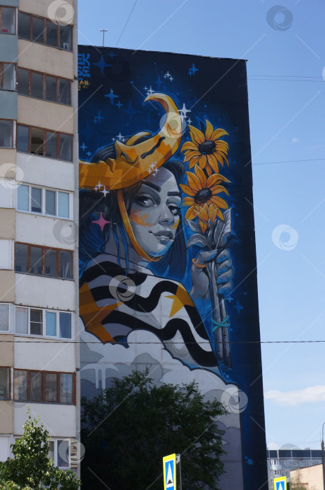 Скачать Казань, Татарстан, Россия - июнь 2023: мурал, изображающий девушку с цветами и в шляпе в форме луны на бульваре "Белые цветы" фотосток Ozero