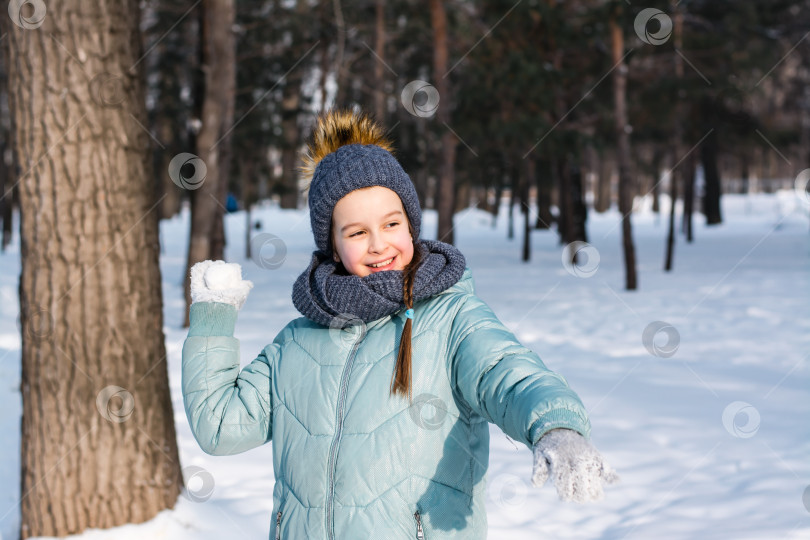 Скачать Веселая девушка в теплой одежде бросает снежок в зимнюю па фотосток Ozero