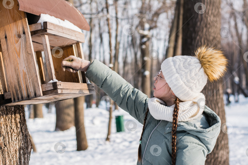 Скачать Подросток насыпает семена в самодельную кормушку для птиц на дереве в фотосток Ozero