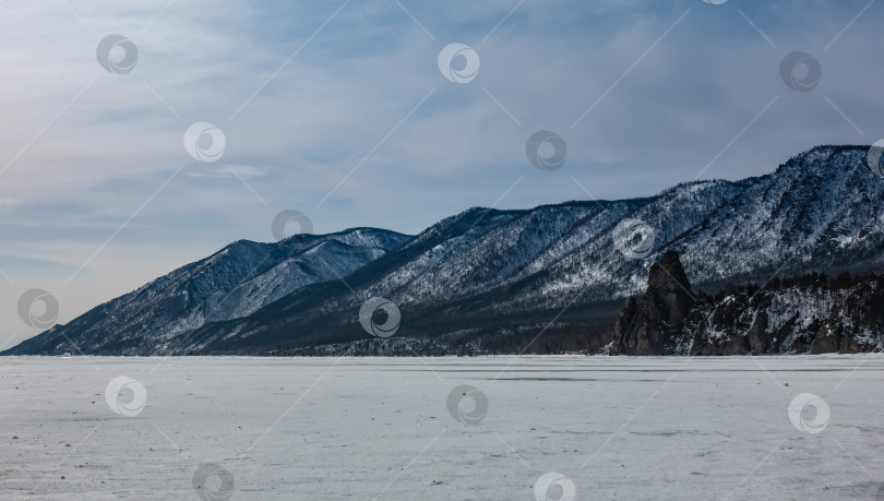 Скачать Замерзшее озеро покрыто снегом. Прибрежный лесистый горный хребет на фоне голубого неба. фотосток Ozero