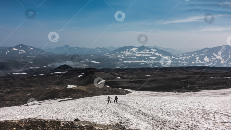 Скачать На горном склоне растаял снег. Два человека с треккинговыми палками отдыхают во время восхождения на вершину. фотосток Ozero