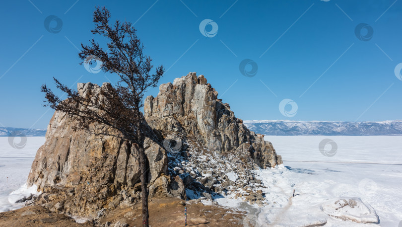 Скачать Двуглавая гранитная скала, лишенная растительности, возвышается над замерзшим, покрытым снегом озером. фотосток Ozero