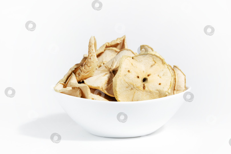 Скачать Сухие яблочные чипсы в белой тарелке, выделенные на белом фоне. Обезвоженная пища. Горсть яблочных чипсов. Здоровая диета для перекусов. фотосток Ozero