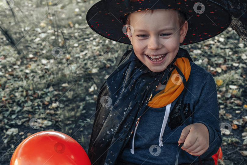 Скачать Дети на Хэллоуин. Милый маленький мальчик, ребенок в шляпе ведьмы с оранжевыми и черными воздушными шариками и ведерком конфет Jack O Lantern. счастливого Хэллоуина. фотосток Ozero