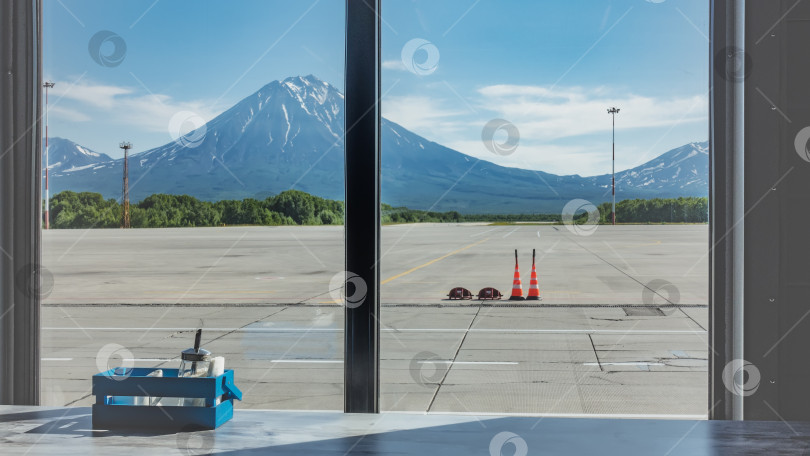 Скачать Из окна кафе аэропорта видна взлетно-посадочная полоса, живописные конусообразные вулканы на фоне неба. фотосток Ozero