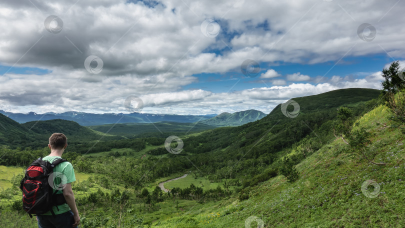 Скачать Турист с рюкзаком стоит на горном склоне, глядя вниз и вперед. фотосток Ozero