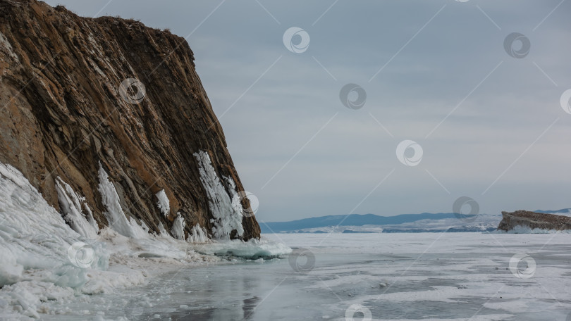 Скачать Отвесная гранитная скала, лишенная растительности, возвышается над замерзшим озером. фотосток Ozero