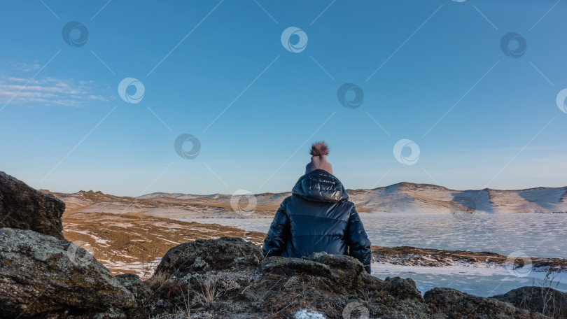 Скачать Девушка в пуховике и шапочке сидит на гранитной скале. фотосток Ozero