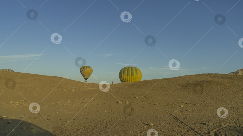 Скачать Яркие воздушные шары поднимаются в голубое небо над песчаными дюнами. фотосток Ozero