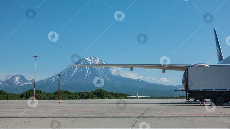 Скачать Самолет стоит на взлетно-посадочной полосе. Крыло на фоне красивого конусообразного вулкана фотосток Ozero