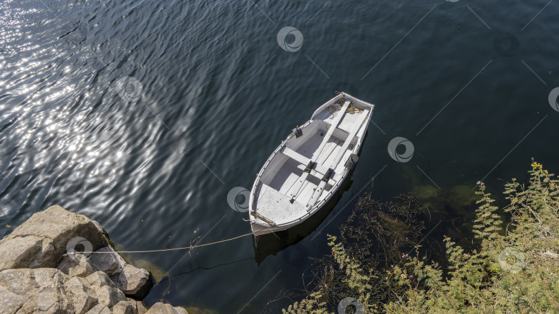 Скачать Белая деревянная лодка привязана к прибрежным валунам. фотосток Ozero