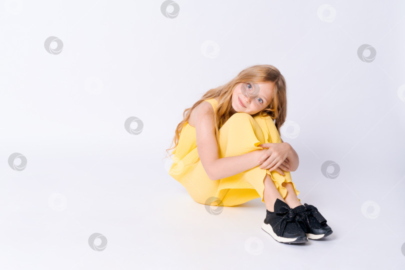 Скачать Студийный портрет симпатичной девушки с вьющимися волосами, сидящей на полу в студии и улыбающейся фотосток Ozero