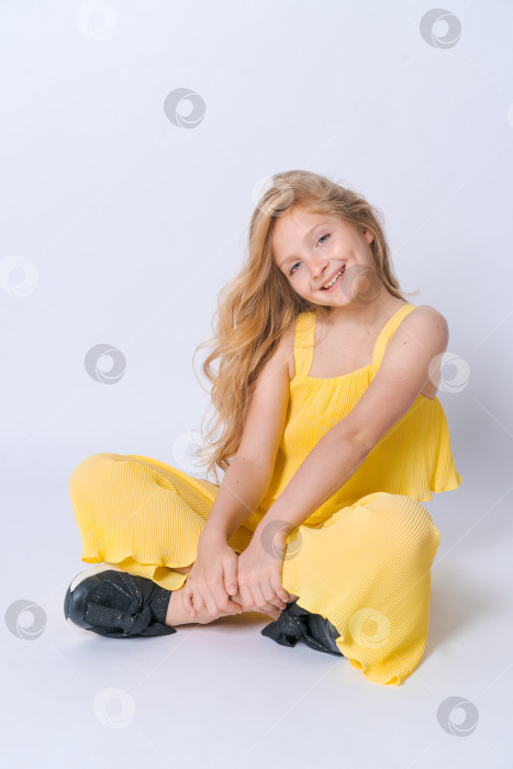 Скачать Студийный портрет симпатичной девушки с вьющимися волосами, сидящей на полу в студии и улыбающейся фотосток Ozero