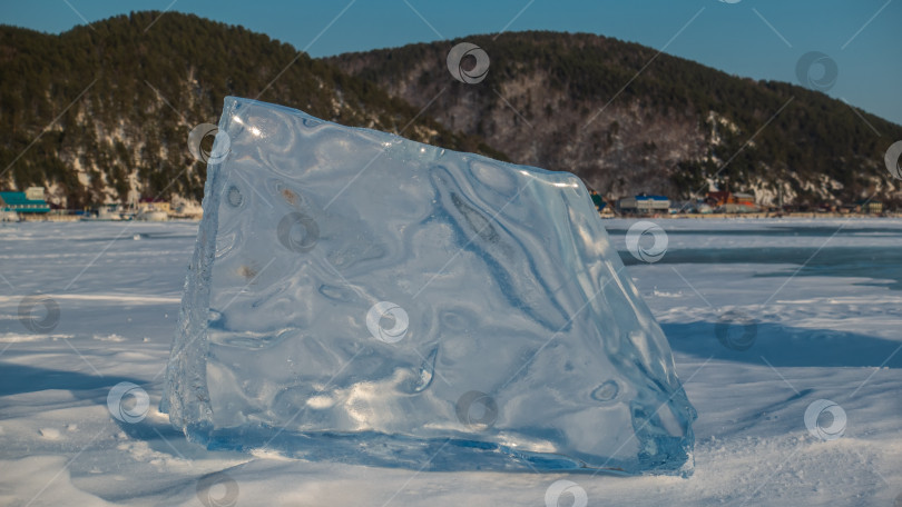Скачать Большая блестящая льдина вертикально стоит на замерзшем и заснеженном озере. фотосток Ozero