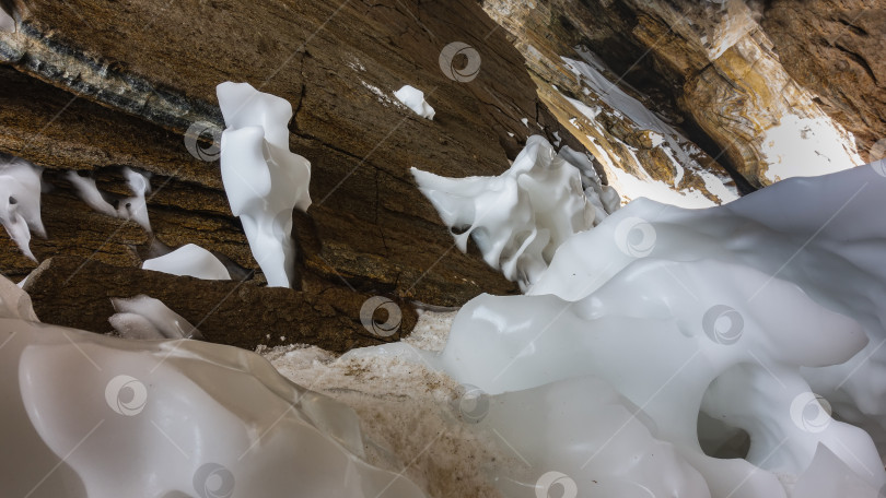 Скачать Ледяные сугробы причудливой формы застыли у подножия гранитной скалы в пещере. фотосток Ozero