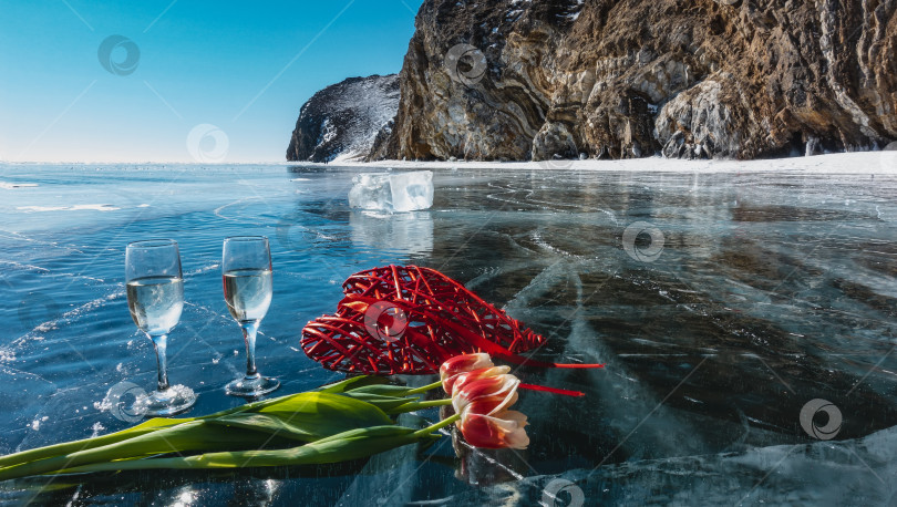 Скачать На голубом льду замерзшего озера Байкал - два бокала шампанского, яркие тюльпаны, красное декоративное плетеное сердечко. фотосток Ozero