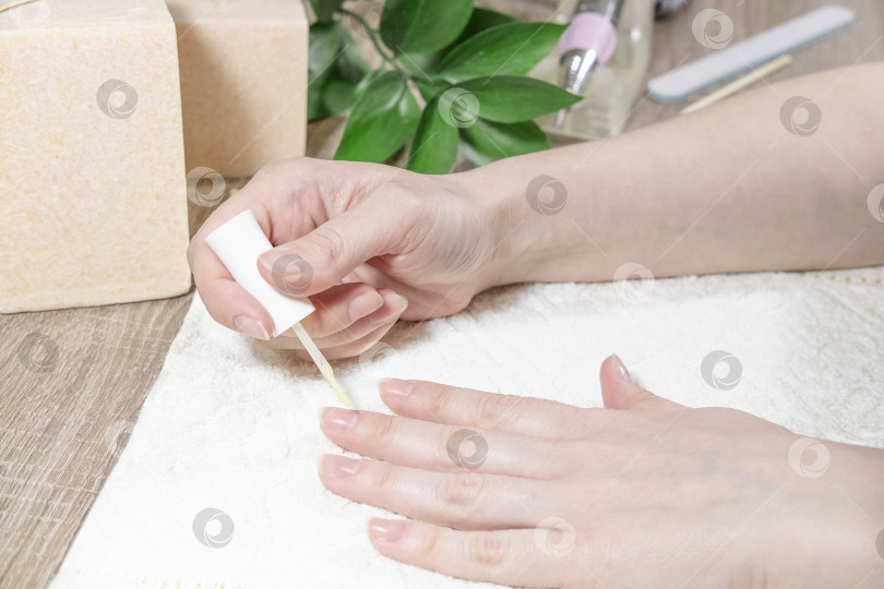 Скачать Женщина-мастер маникюра покрывает свои ногти защитным покрытием, лаком для ногтей или гель-лаком, используя бежевое прозрачное средство в салоне красоты. Процесс маникюра или нанесение лака на ногти крупным планом. фотосток Ozero